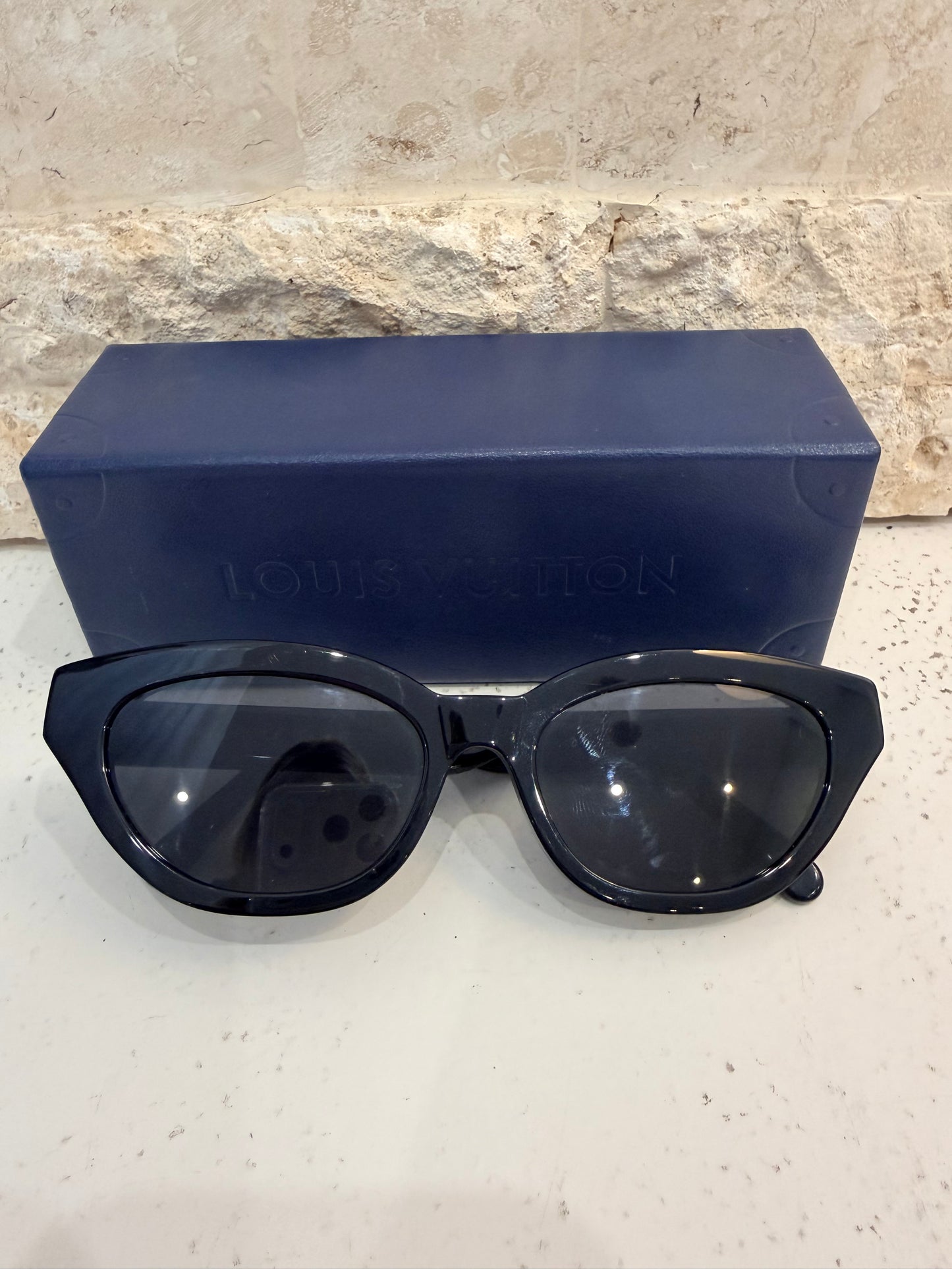 Black sunglasses on a light stone surface with a blue case.