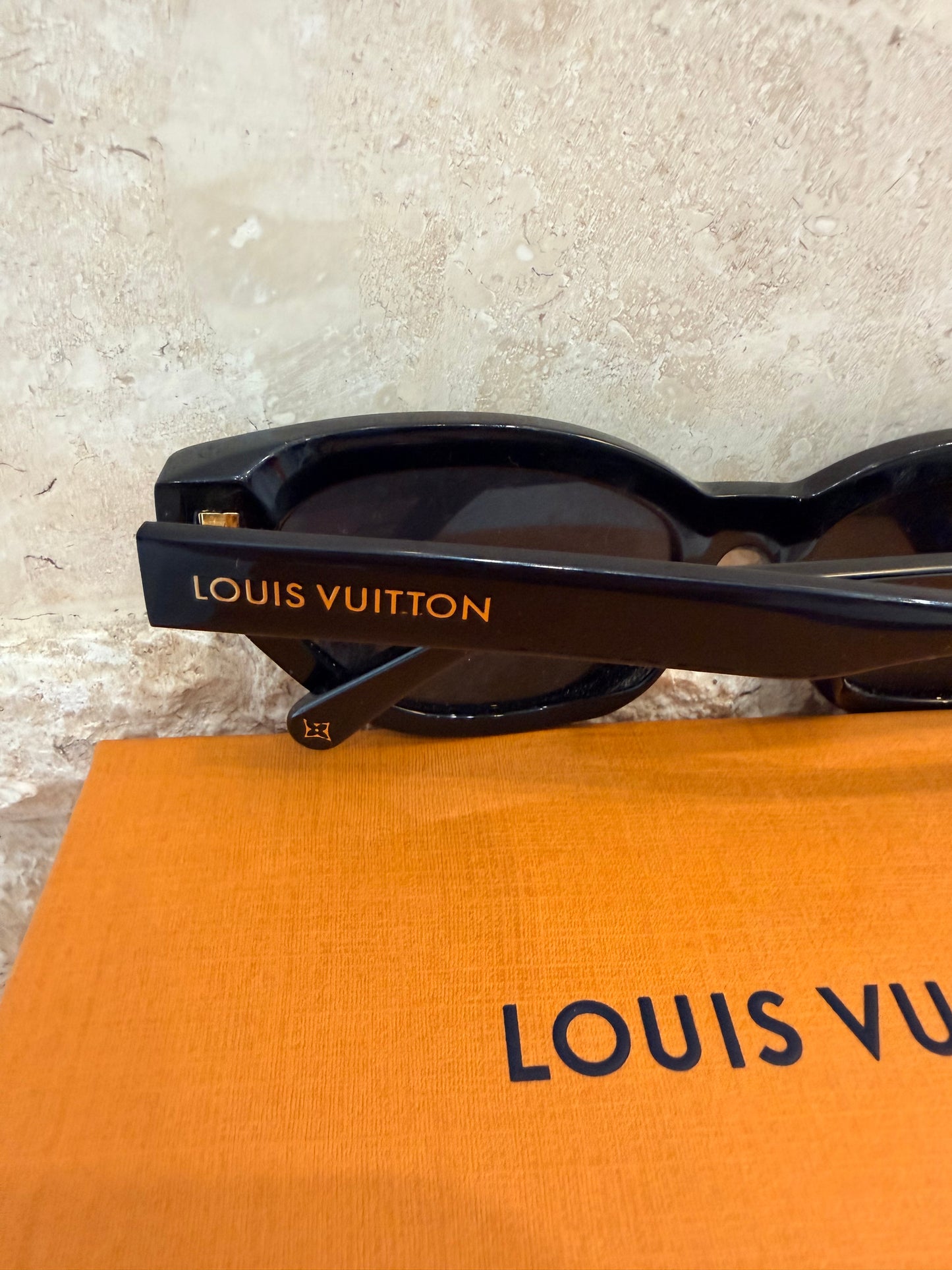 Louis Vuitton sunglasses on a textured surface with an orangeLouis Vuitton pouch underneath.